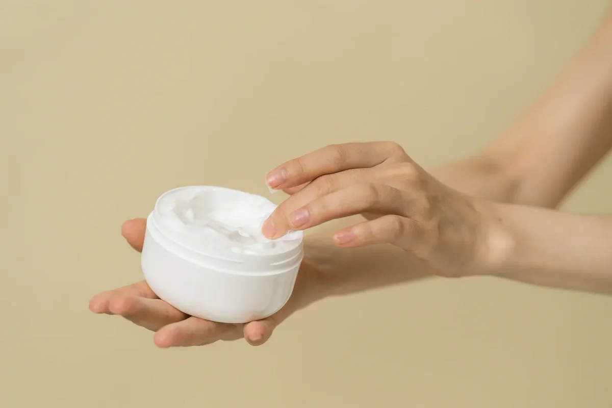 Pot de crème de soin pour la peau avec application sur une main féminine