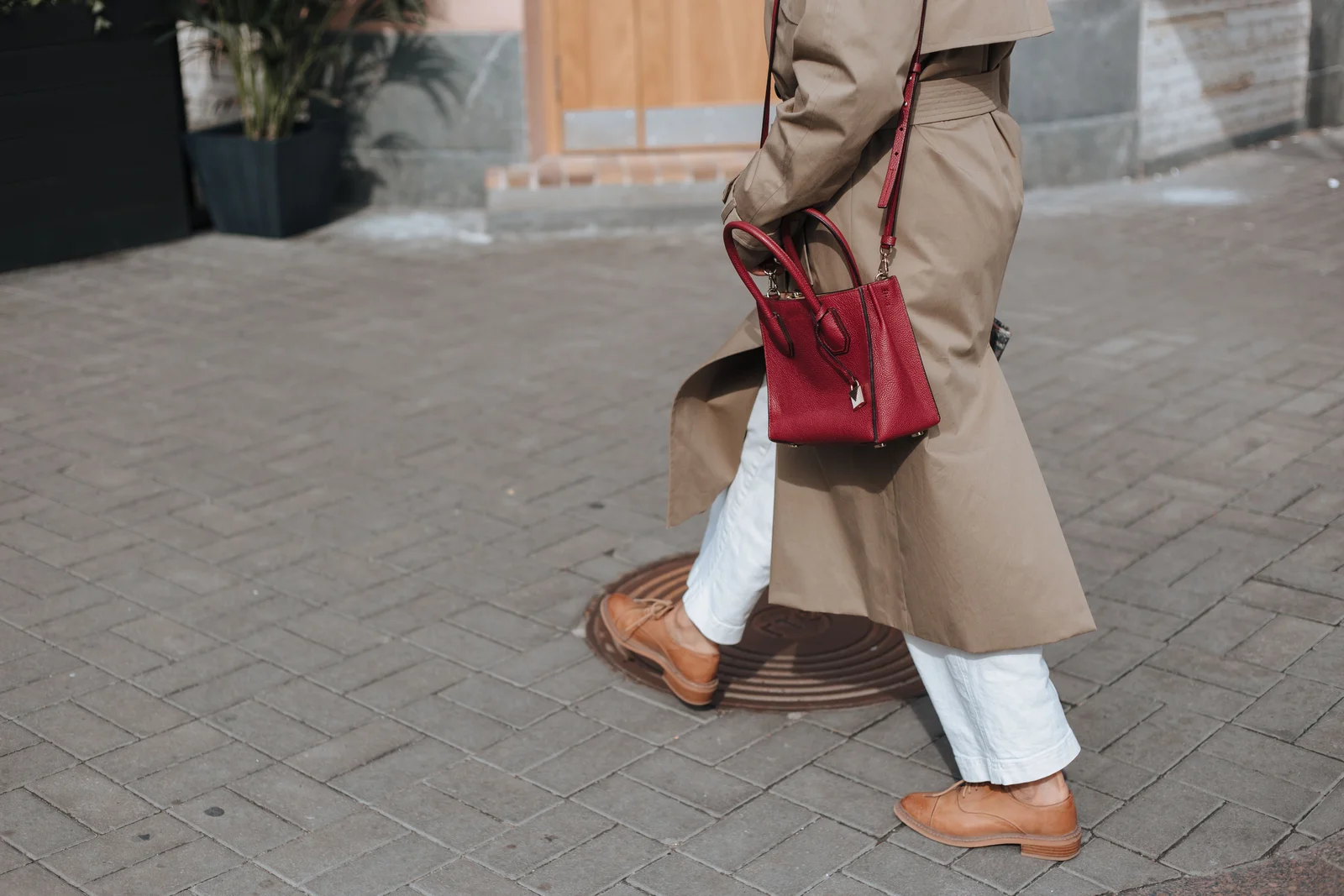 Femme en trench beige portant un sac à main rouge à la main, marchant en rue