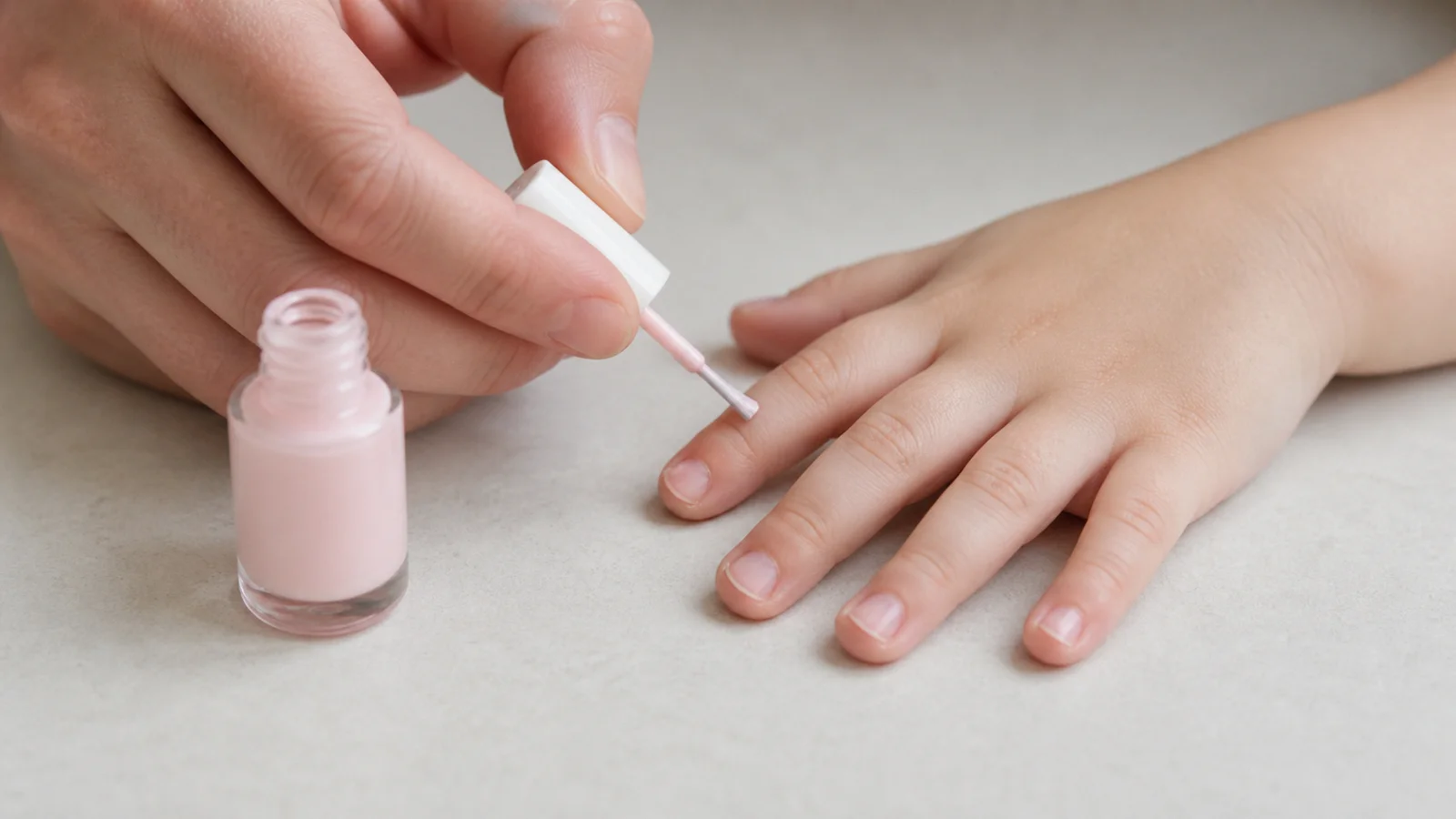 Pose d'un vernis rose pâle au pinceau sur les ongles courts d'un enfant